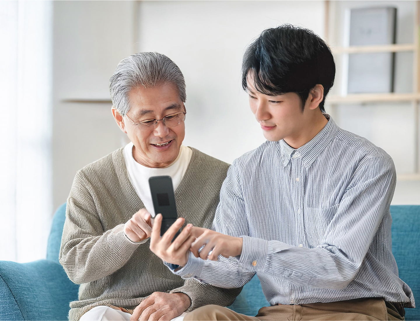 祖父と一緒にらくらくホンを見る孫